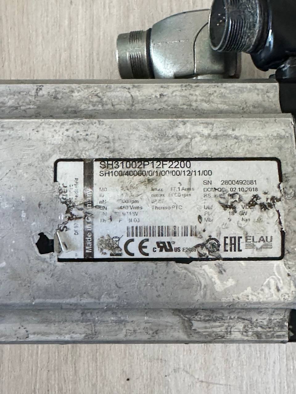 Крупный план потертого заводского шильдика промышленного серводвигателя Schneider Electric SH31002P12F2200. Считывание номинальных характеристик электромотора перед проведением стендовой диагностики и компонентного ремонта.