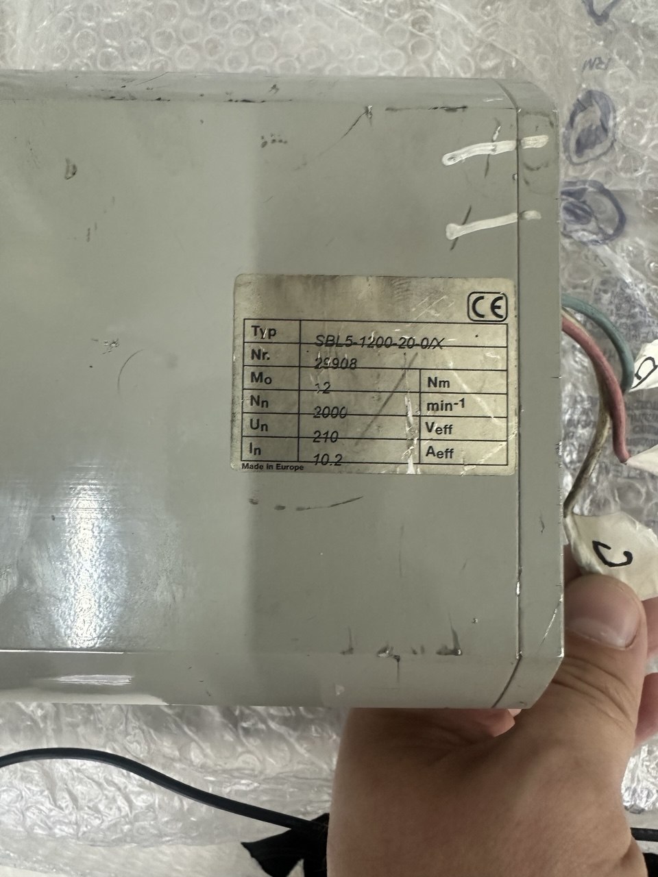 Крупный план информационной таблички промышленного серводвигателя SMB SBL5-1200-20-0/X. На металлическом шильдике указаны основные заводские параметры: номинальный крутящий момент 12 Nm, скорость вращения 2000 мин-1, напряжение 210 Veff и ток 10.2 Aeff.