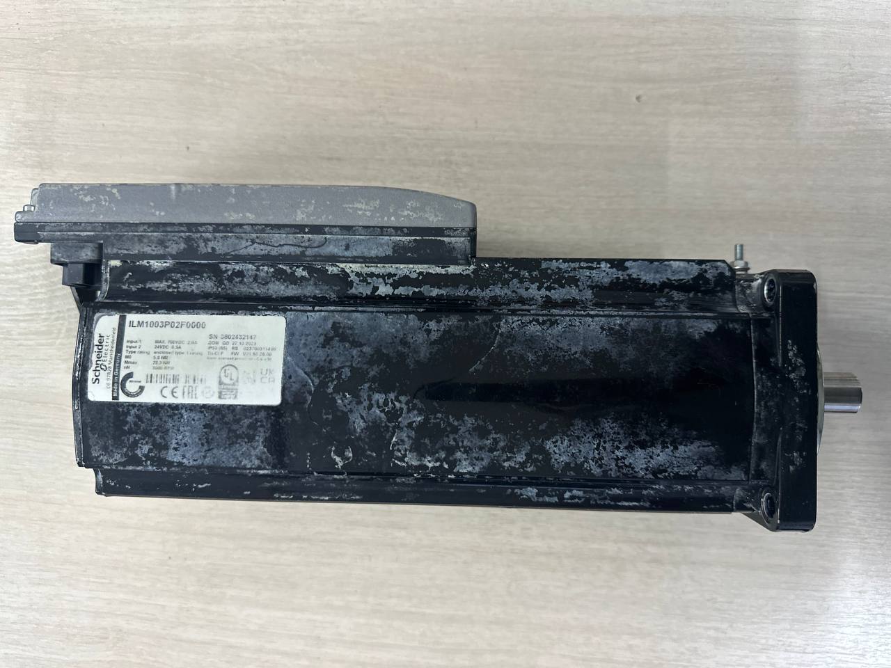 Интегрированный серводвигатель Schneider Electric Lexium ILM1003P02F0000, поступивший в сервисный центр на ремонт. На черном корпусе видны следы интенсивной промышленной эксплуатации (отслоение краски, потертости) и заводская информационная табличка с характеристиками.
